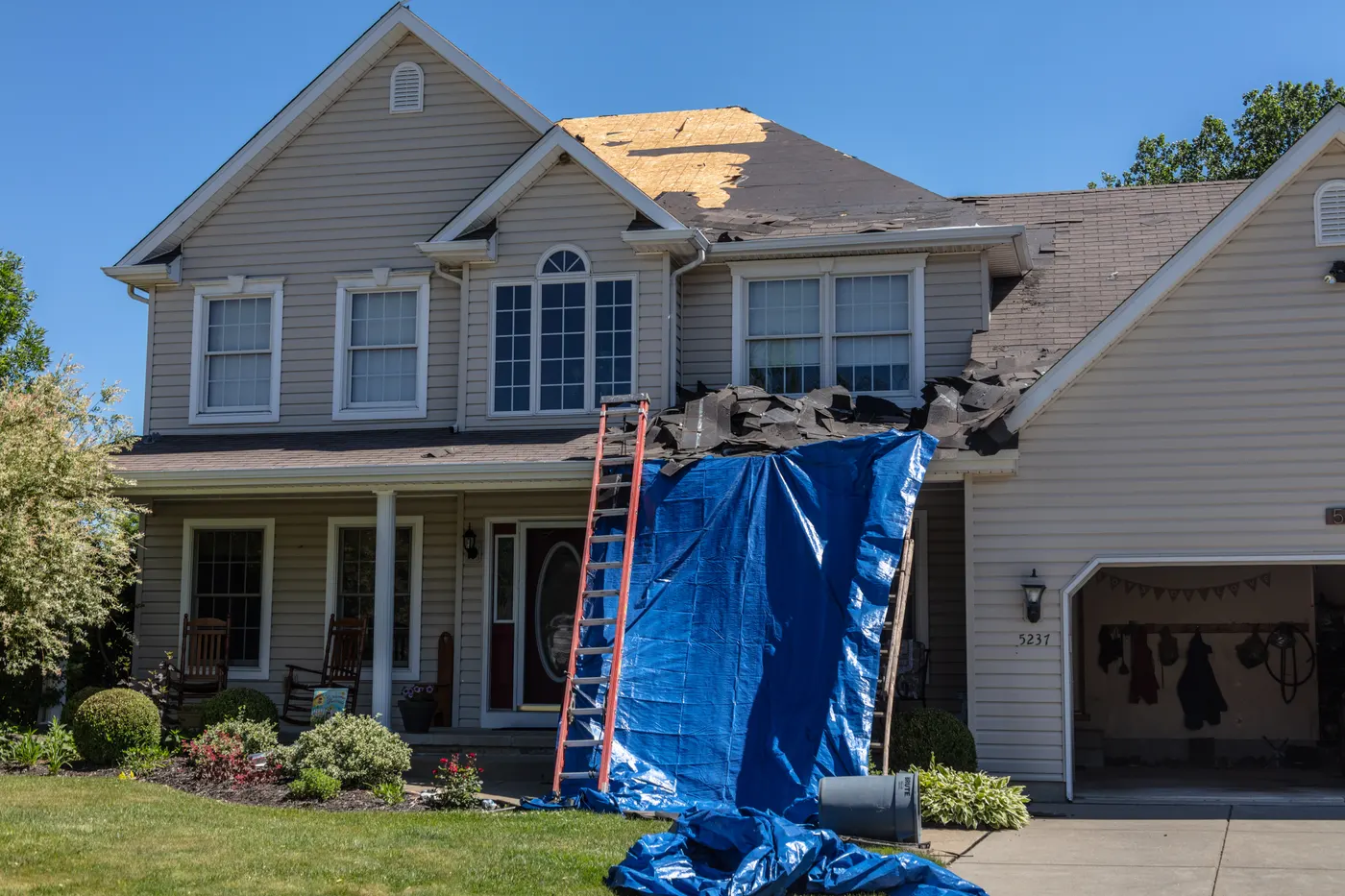 A colonial house with a ladder and tarp up for roof work