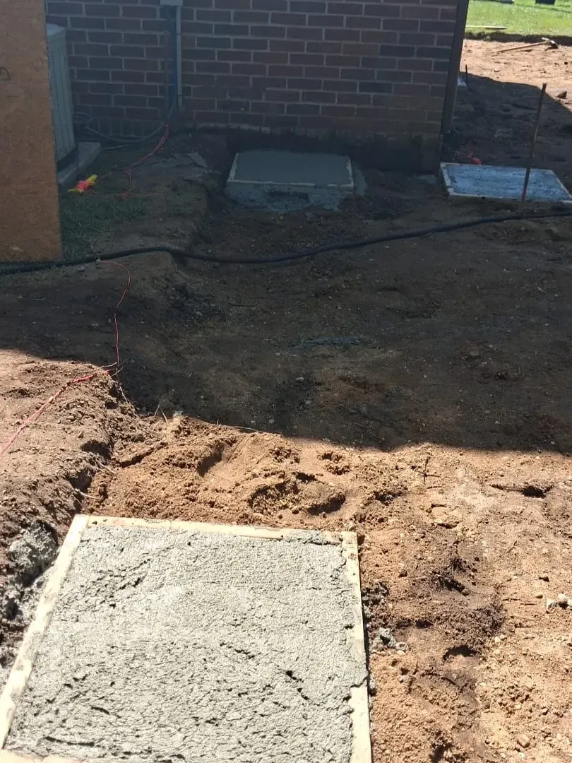 A freshly poured concrete footing beside a foundation