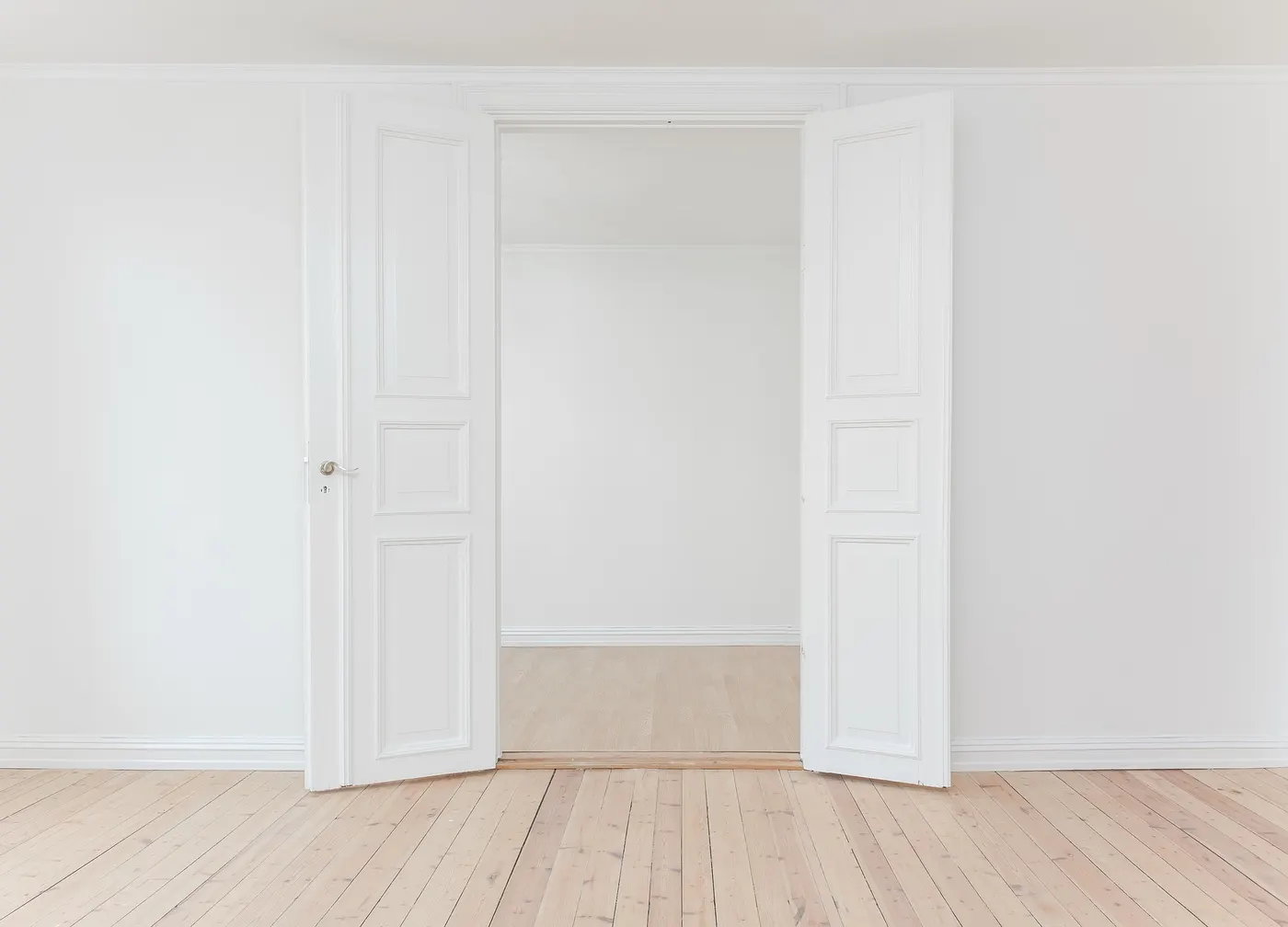 A freshly finished room with a new wood floor and white double doors