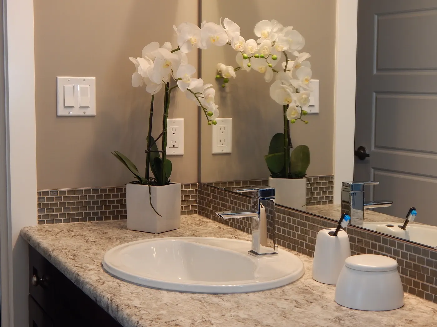 A remodeled bathroom vanity with a stone countertop and tiled backsplash