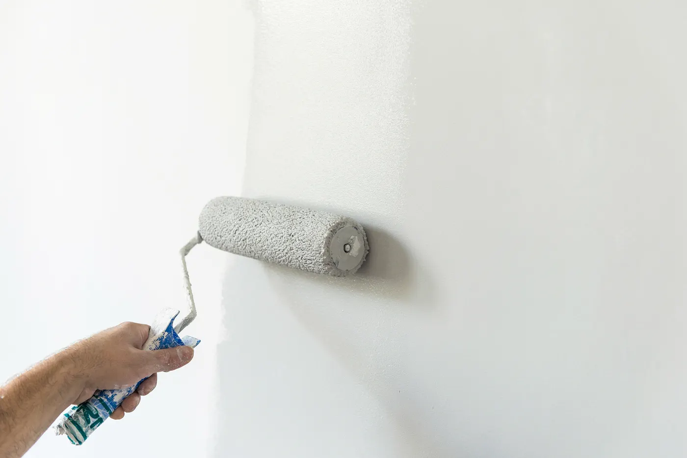 A painter rolling white paint onto an interior wall